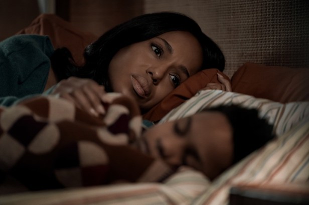 "Woman lying in bed looking thoughtful while a child sleeps beside her, both under a patterned blanket in a cozy, softly lit bedroom setting."